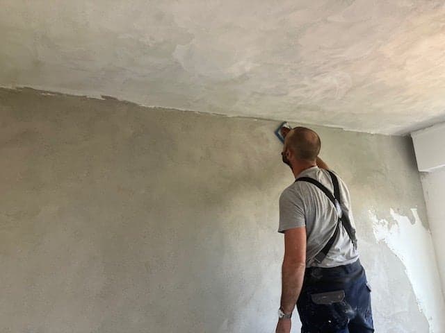Florian lissant un enduit à la main en haut d'un mur